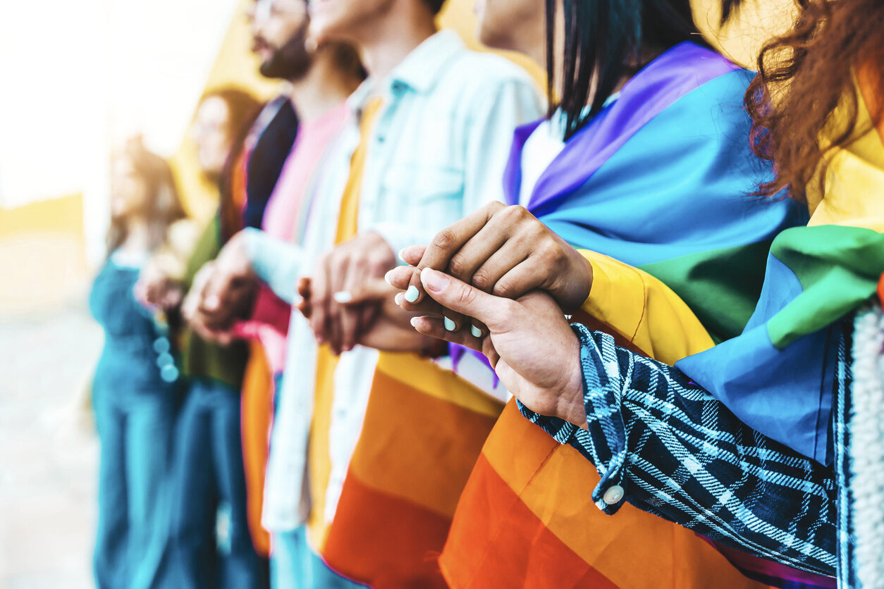 Group of lgbt people holding hands outside - Diverse happy friends hugging outdoors - Gay pride concept with crowd of guys and girls standing together on city street